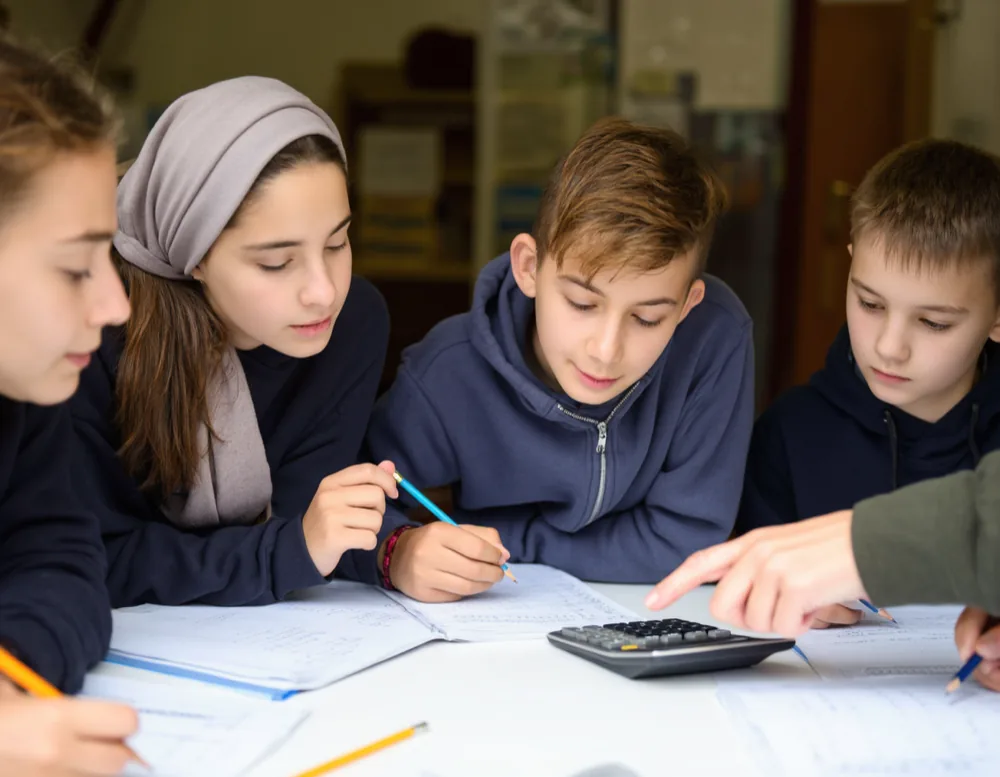 Four primary and secondary pupils working on maths exercise books at a shared table
