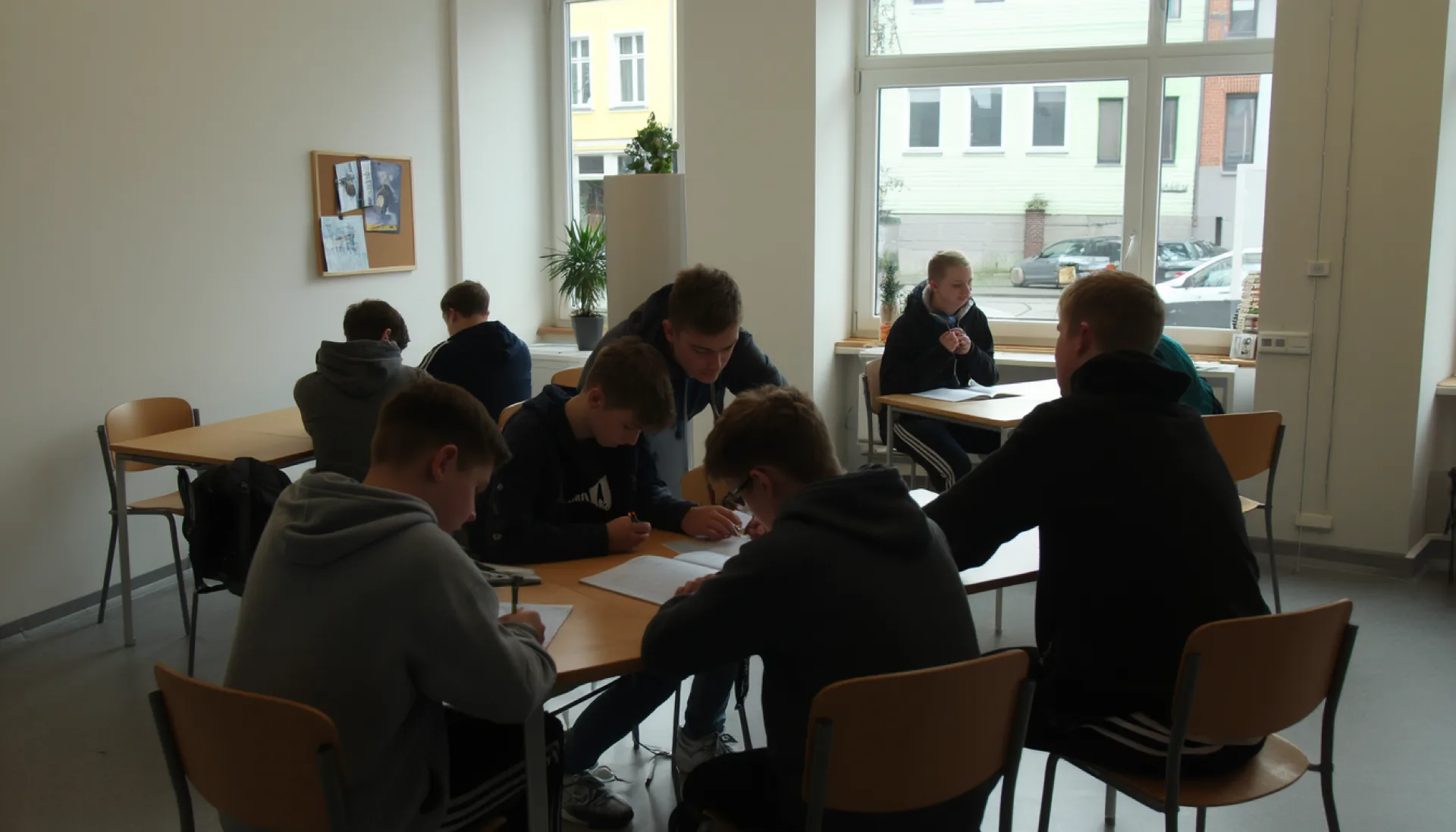 Pupils in hoodies working together at two long shared tables in the Lernkiste shop unit, daylight coming in from the street window